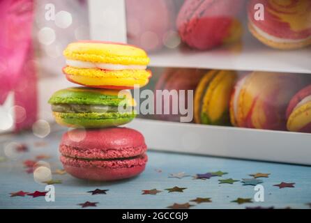 Macarons colorés et boîte de guimauve ornée d'un noeud rouge sur une table en bois. Composition de fête ou d'anniversaire avec bokeh Banque D'Images