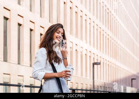 portrait horizontal d'une jeune femme indienne attrayante parlant au téléphone. Elle se trouve près de l'immeuble de bureaux Banque D'Images