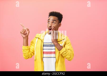 Sans voix, un homme afro-américain intrigué et excité avec une barbe et une coiffure afro disant wow and gasting tenant la paume près de la bouche ouverte regarder et Banque D'Images