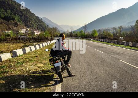 homme assis à moto sur la route du tarmac avec une belle vue naturelle le matin image est prise au shergaon arunachal pradesh inde. Banque D'Images