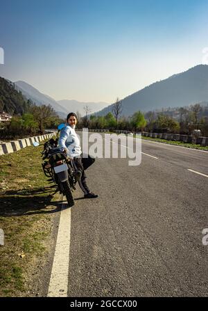 une jeune fille assise à moto sur la route du tarmac avec une belle vue naturelle le matin, image est prise au shergaon arunachal pradesh inde. Banque D'Images