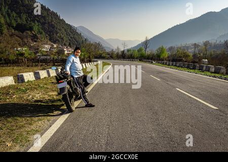 une jeune fille assise à moto sur la route du tarmac avec une belle vue naturelle le matin, image est prise au shergaon arunachal pradesh inde. Banque D'Images