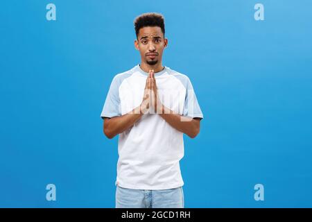 Aidez-moi à vous supplier. Charmant petit ami afro-américain mignon et charmant avec coupe de cheveux et barbe frino-maurille tenant les mains dans la prière faire froid Banque D'Images