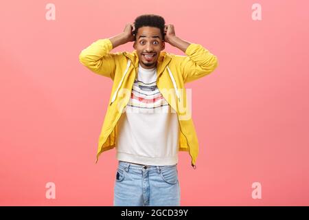 Prise de vue à la taille d'un homme africain de style, nerveux et enthousiaste, avec une coiffure afro tenant les mains près de la tête, en se crampant aux dents et en se fixant Banque D'Images