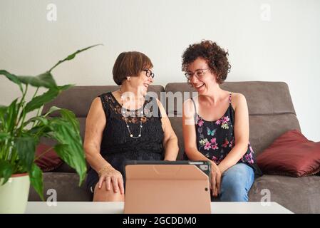 Une jeune femme et sa mère âgée rient tout en regardant du contenu en ligne via une tablette numérique Banque D'Images