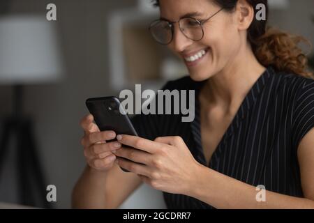 Gros plan femme souriante dans des lunettes à l'aide d'un smartphone, en naviguant dans des applications Banque D'Images