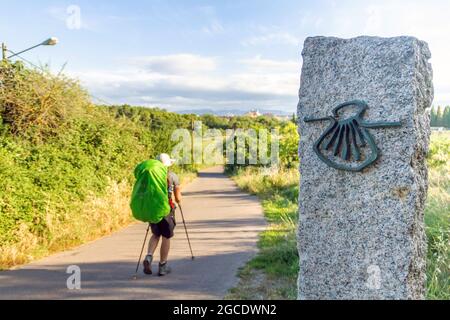 Pèlerin marche le long de la Camino de Santiago (chemin Sant James) portant un sac à dos à côté d'une colonne avec le symbole de la coquille du Camino Santiago de Compo Banque D'Images