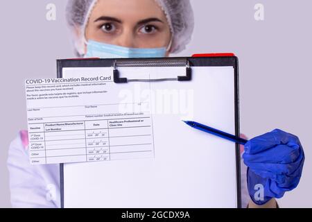 Photo en gros plan de la certification du vaccin sur le porte-document et la femme assistante médicale en uniforme avec le masque facial portant des gants et Banque D'Images