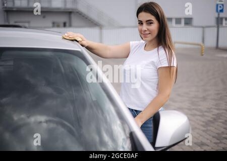 Attrayante heureuse joyeuse femme pilote essuie le pare-brise sur sa voiture en utilisant un chiffon dans le lavage de voiture libre-service Banque D'Images