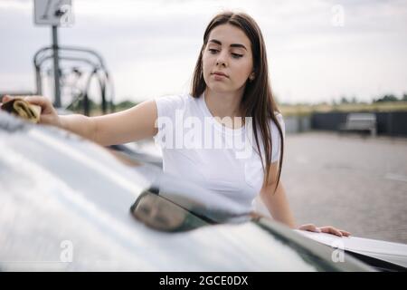 Attrayante heureuse joyeuse femme pilote essuie le pare-brise sur sa voiture en utilisant un chiffon dans le lavage de voiture libre-service Banque D'Images