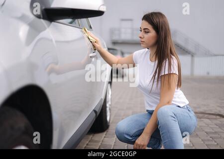 Attirante heureuse heureuse femme pilote essuyez sa voiture à l'aide d'un chiffon dans le lave-auto libre-service Banque D'Images