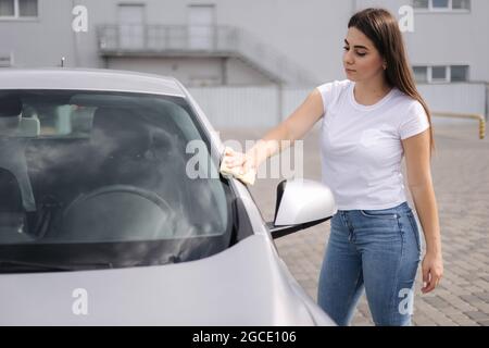 Attirante heureuse heureuse femme pilote essuyez sa voiture à l'aide d'un chiffon dans le lave-auto libre-service Banque D'Images