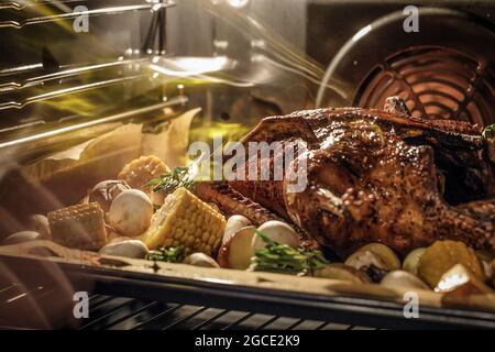 Canard entier sur une plaque de cuisson avec du maïs, des herbes, des champignons et des pommes de terre cuisant dans un four électrique domestique Banque D'Images