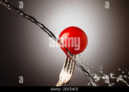tomate cerise sur une fourchette d'argent, jet d'eau, pulvérisation Banque D'Images