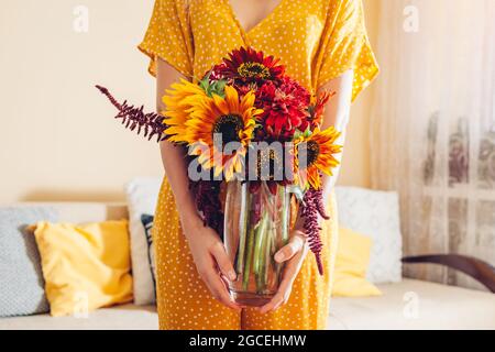 Femme tient vase avec des fleurs de soleil amaranth et des fleurs de zinnia. Bouquet d'automne rouge jaune orange brun fleurs à la maison. Banque D'Images