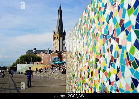 Les gens se détendent sur les marches de la promenade du Rhin à Düsseldorf, en Allemagne. Mur en mosaïque coloré « Rivertime » par Hermann-Josef Kuhna. Banque D'Images