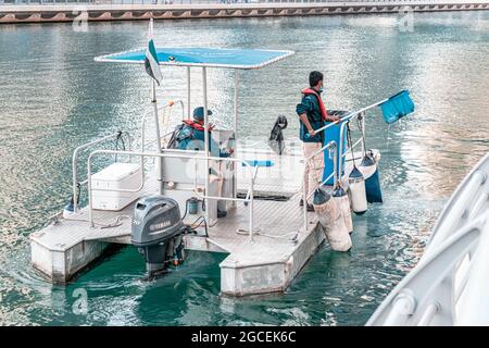 21 février 2021, Dubaï, Émirats arabes Unis : employés de services municipaux sur un bateau à moteur avec un filet de capture des ordures de la baie dans la Marina de Dubaï Banque D'Images