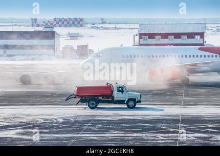 En hiver, un camion avec du carburant ou de l'eau se déplace sur la voie de circulation de l'aéroport contre le fond d'un avion fumeur. Concept d'un incident dangereux an Banque D'Images