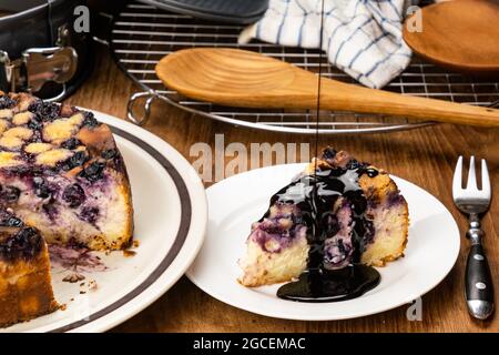 Verser la garniture de chocolat sur un morceau de délicieux bleuet maison et cheesecake crumble dans un plat en céramique blanche avec un grand dans un plat brun, en bois Banque D'Images