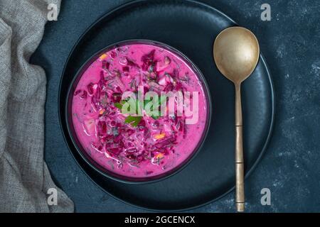 Délicieuse soupe froide de betteraves avec concombre, œuf dur, radis dans un bol noir sur la table, gros plan, vue du dessus Banque D'Images