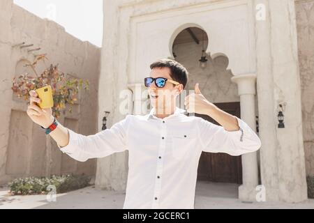 Un homme heureux sourit et prend un selfie ou un blog vidéo d'enregistrement sur le fond d'une tour de vent dans le vieux quartier de Bur Dubai Creek. Voyages et soc Banque D'Images