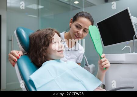 Adorable jeune garçon vérifiant les dents dans le miroir après la procédure dentaire au bureau de dentistes Banque D'Images