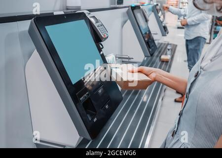 Femme lit le code-barres de sa boîte à lunch pour un paiement sans espèces à la caisse libre-service du supermarché. Ces kiosques de machines permettent d'augmenter thr Banque D'Images