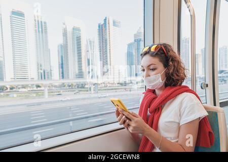 Une femme passager portant un masque médical se déplace dans les transports publics et lit les nouvelles ou utilise une application sur son smartphone. Le concept de coronavirus restr Banque D'Images