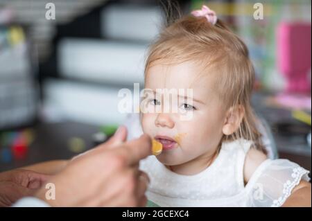 Un homme attentionné nourrit sa petite fille. Portrait d'une petite fille assise à la table du dîner des enfants et déjeuner avec son père. Heureux Banque D'Images