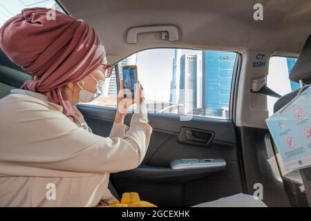 23 février 2021, Dubaï, Émirats arabes Unis : une femme musulmane prend des photos des gratte-ciels de Dubaï sur son smartphone depuis la fenêtre d'une voiture Banque D'Images