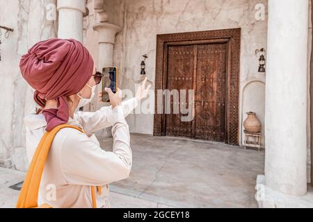 Une femme heureuse portant un masque prend des photos sur son smartphone sur le fond d'une vieille ville de Bur Dubai près du quartier de Creek Banque D'Images