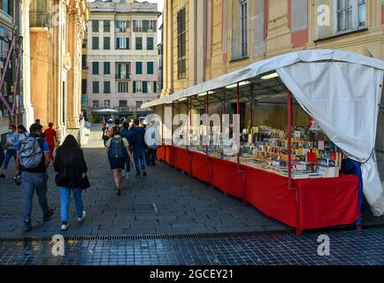 Un stand de livre d'occasion dans le marché de rue d'un côté du Palais Ducal sur la place de Ferrari avec des touristes en été, Gênes, Ligurie, Italie Banque D'Images