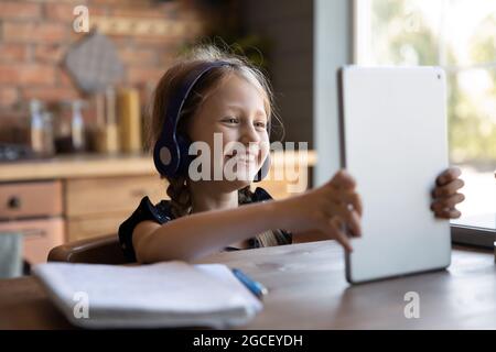 Joyeux élève de l'école qui porte des écouteurs, en utilisant une tablette Banque D'Images