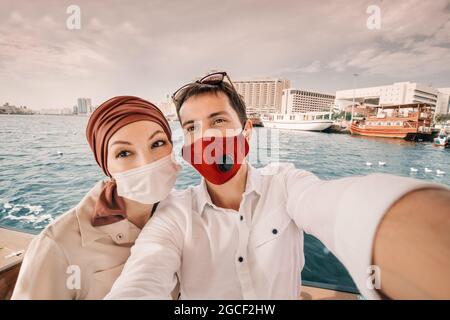 Homme et femme portant un masque médical voyageant sur le ferry traditionnel Abra Dhow sur la crique de Dubaï et prenant une photo de selfie. Coronavirus et covid Banque D'Images