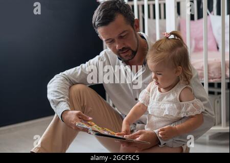 Un père attentionné lit un conte de fées à sa petite fille dans la chambre des enfants. Banque D'Images