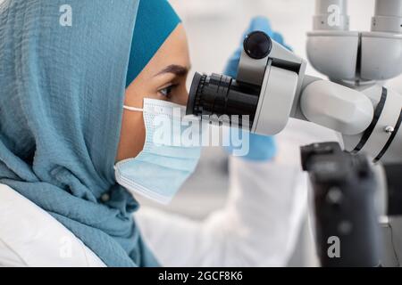 Femme musulmane travailleur médical regardant dans le microscope, faisant la recherche en laboratoire, la Dame islamique dans le hijab et masque de protection du visage analyse de la amp de sang Banque D'Images