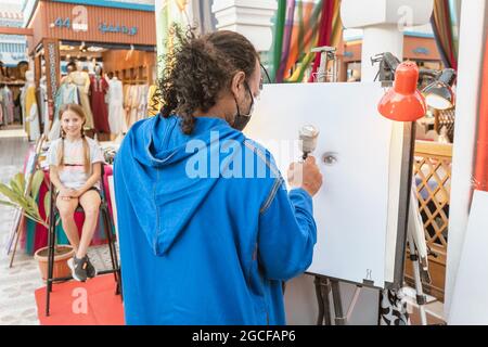 26 février 2021, eau, Dubaï : un artiste de rue peint son client sur toile à l'aide d'un aérographe Banque D'Images