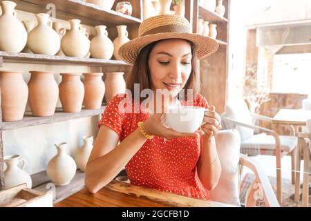 Une femme d'apparence indienne ou indonésienne boit le thé ou le café d'une grande tasse dans un café sur fond de poterie comme décor Banque D'Images