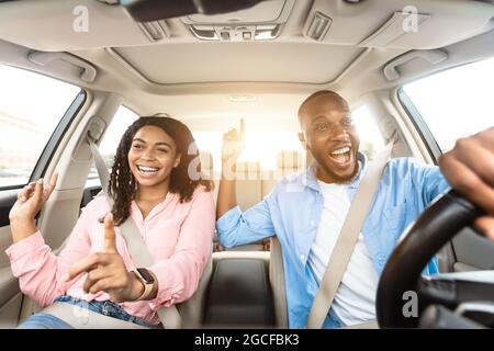 Concept de Road Trip. Portrait de face d'un couple afro-américain amusant et enthousiaste conduisant une voiture de luxe, dansant sur la musique et chantant la chanson préférée, reposez-vous Banque D'Images