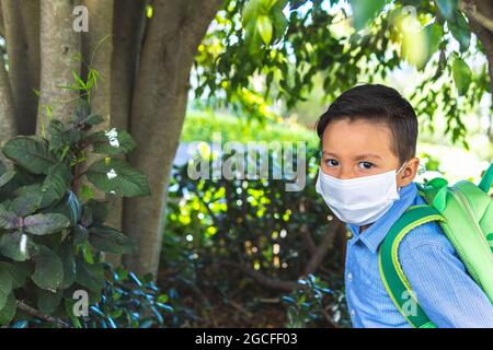 Portrait d'un garçon latino avec un masque et un sac à dos au milieu de la végétation. Retour à l'école Banque D'Images