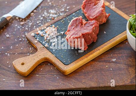 L'herbe de Hereford crue a nourri le filet de bœuf sur une plaque de salade noire avec du sel, un couteau et une tasse de salade de roquette Banque D'Images