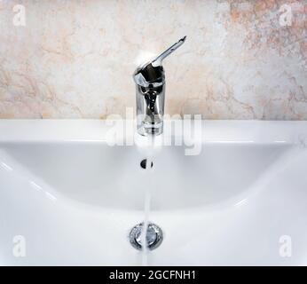 Robinet chromé avec levier pour mélanger de l'eau chaude et froide sur un lavabo blanc moderne dans une salle de bains avec des murs carrelés. Vie domestique et hygiène Banque D'Images