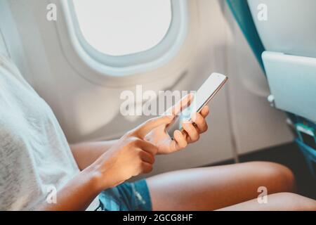 Téléphone portable avec une femme en vol. Passager de l'avion utilisant l'écran de l'application de téléphone mobile pour une preuve de passeport de vaccin à l'arrivée à l'aéroport pour un voyage de vacances Banque D'Images