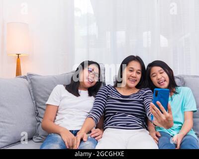 Une famille heureuse assise sur un canapé dans la salle de séjour parle avec quelqu'un sur un téléphone mobile ensemble, une mère souriante montrant un mignon petit enfant appel vidéo par smartp Banque D'Images