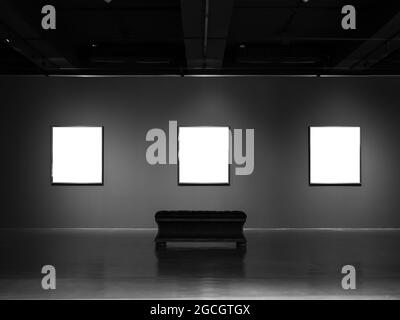 Trois cadres d'art de musée blanc maquette sur fond de mur gris foncé avec éclairage et banc de siège vide. Banque D'Images
