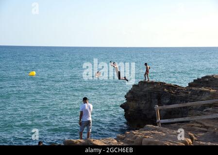 Roda de Bara, Espagne. 05 août 2021. Un jeune homme plonge dans la mer depuis une falaise à la plage du Roc de Sant Gaieta à Roda de Bara.les jeunes sautent des falaises à la plage du Roc de Sant Gaieta à Roda de Bara (Tarragone Espagne), une pratique qui est interdite, dangereux et peut causer de graves blessures corporelles et même la mort par l'impact contre les roches. Crédit : SOPA Images Limited/Alamy Live News Banque D'Images