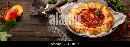 Galette de pêche sur papier de cuisson sur fond en bois. Tarte maison fraîchement préparée. panorama Banque D'Images