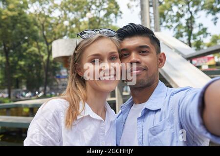 Joyeux sourire divers couple prenant le selfie sur un smartphone lorsqu'ils marchent en ville où ils se sont rendus Banque D'Images