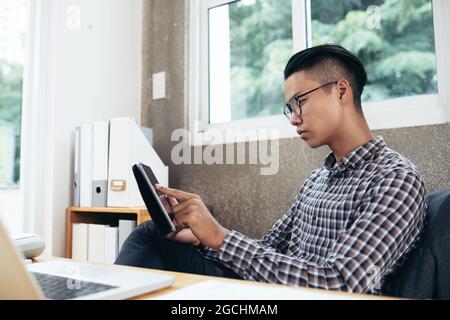 Homme d'affaires sérieux travaillant à la table de bureau, il est en train de lire un document ou d'utiliser une application sur un ordinateur tablette Banque D'Images