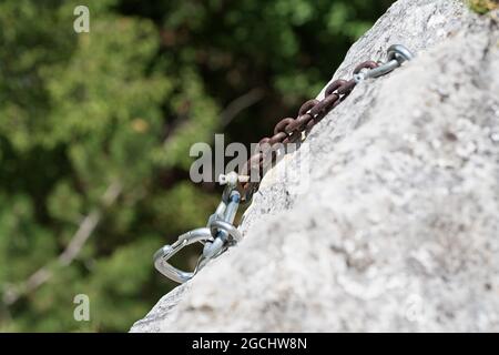 Mousqueton grimpant sur une chaîne en acier rouillé attachée à la roche au-dessus du précipice. Escalade, équipement et concepts de sécurité Banque D'Images